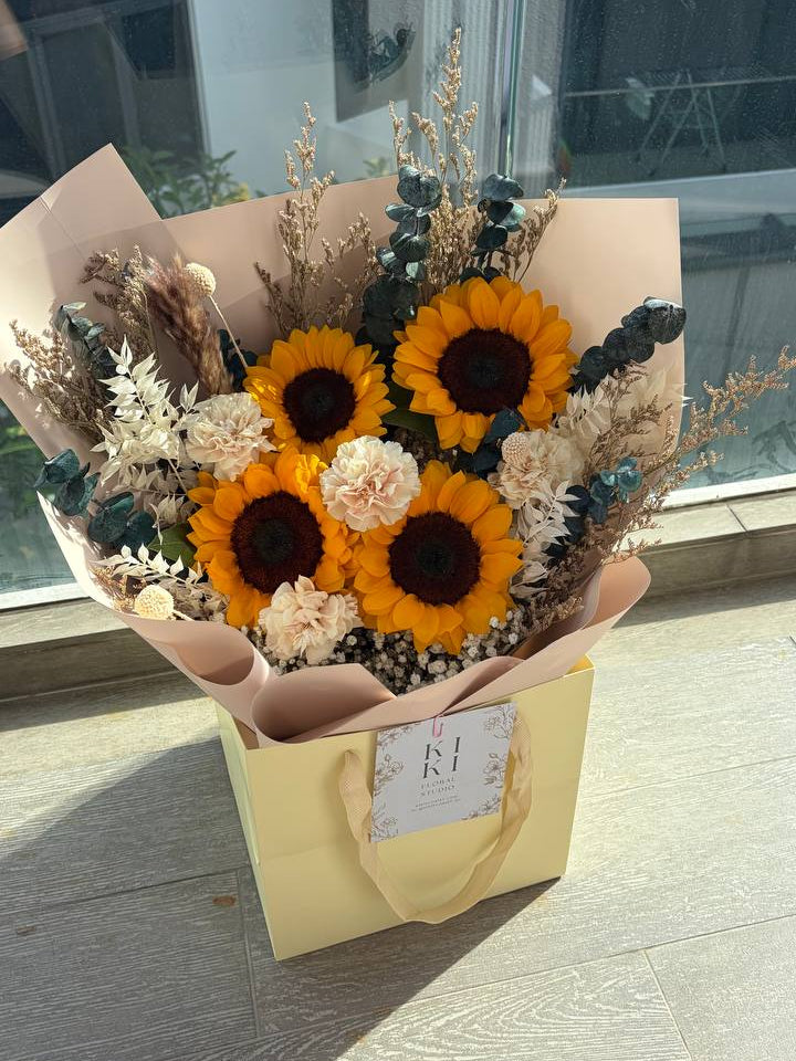 Bouquet of sunflowers and dried flowers in a yellow box on a concrete floor.