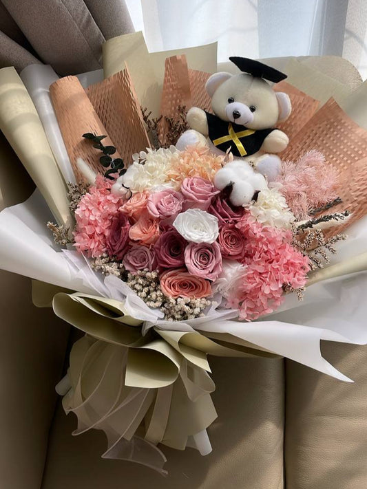 Bouquet of flowers with a teddy bear wearing a graduation cap and gown in a room.