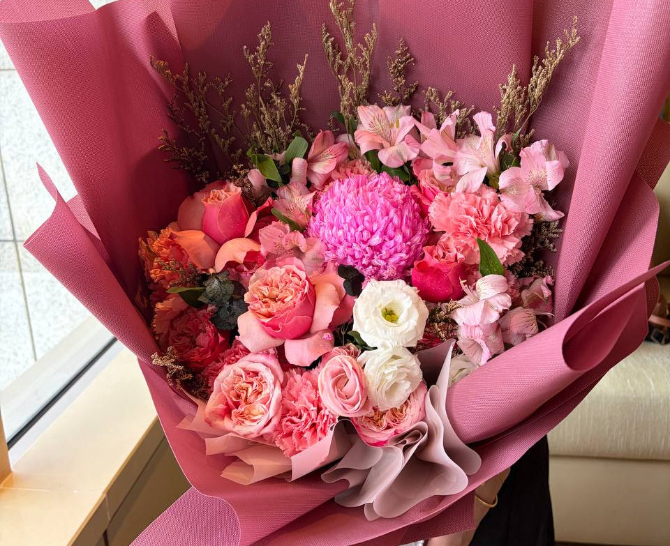 Bouquet of flowers wrapped in pink paper held by a person indoors.