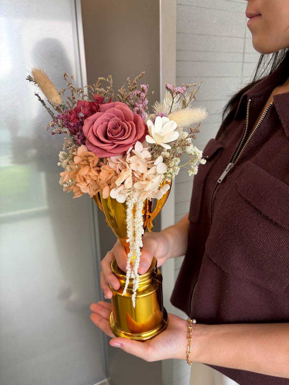 Person holding a bouquet of flowers in a gold vase.